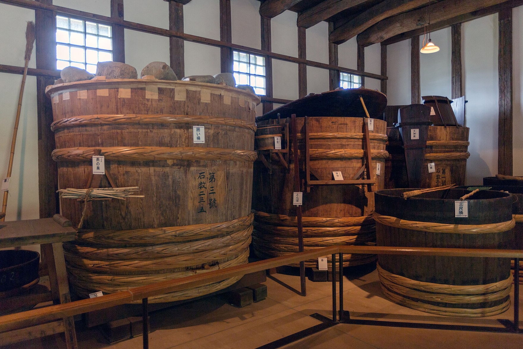 Tall cedar vats bound with bamboo hoops standing in a timber-framed sake brewery