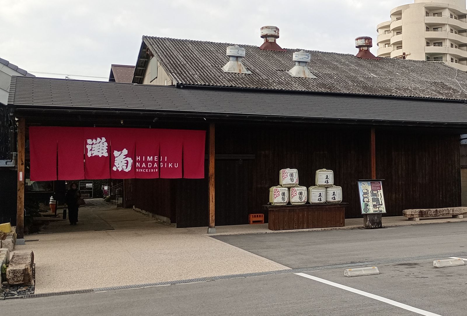 The dark timber frontage of Nadagiku sake brewery in Himeji, with a red noren curtain and stacked sake barrels